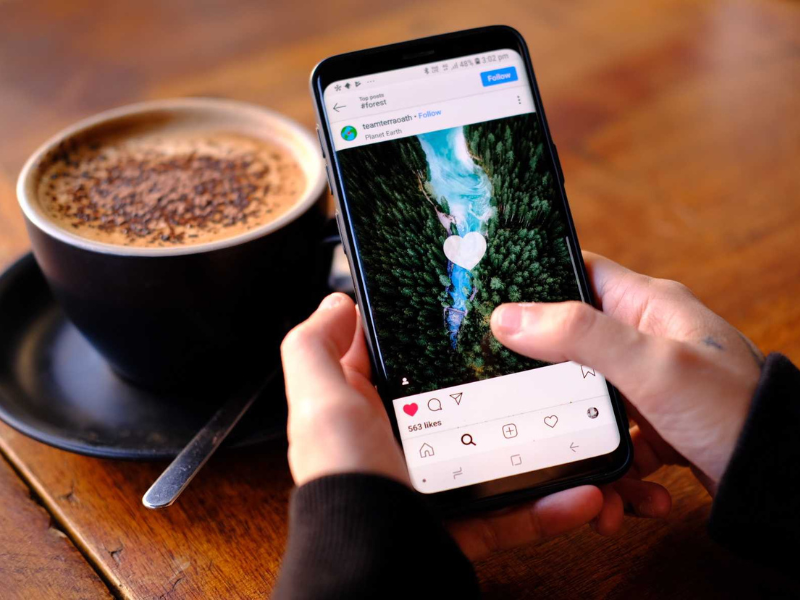 Persona gestionando Instagram con una estética náutica en el móvil, acompañada de una taza de café.