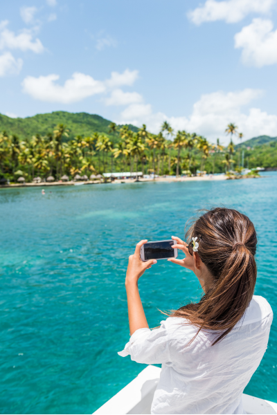 Mujer fotografiando una playa tropical desde un barco en aguas turquesas