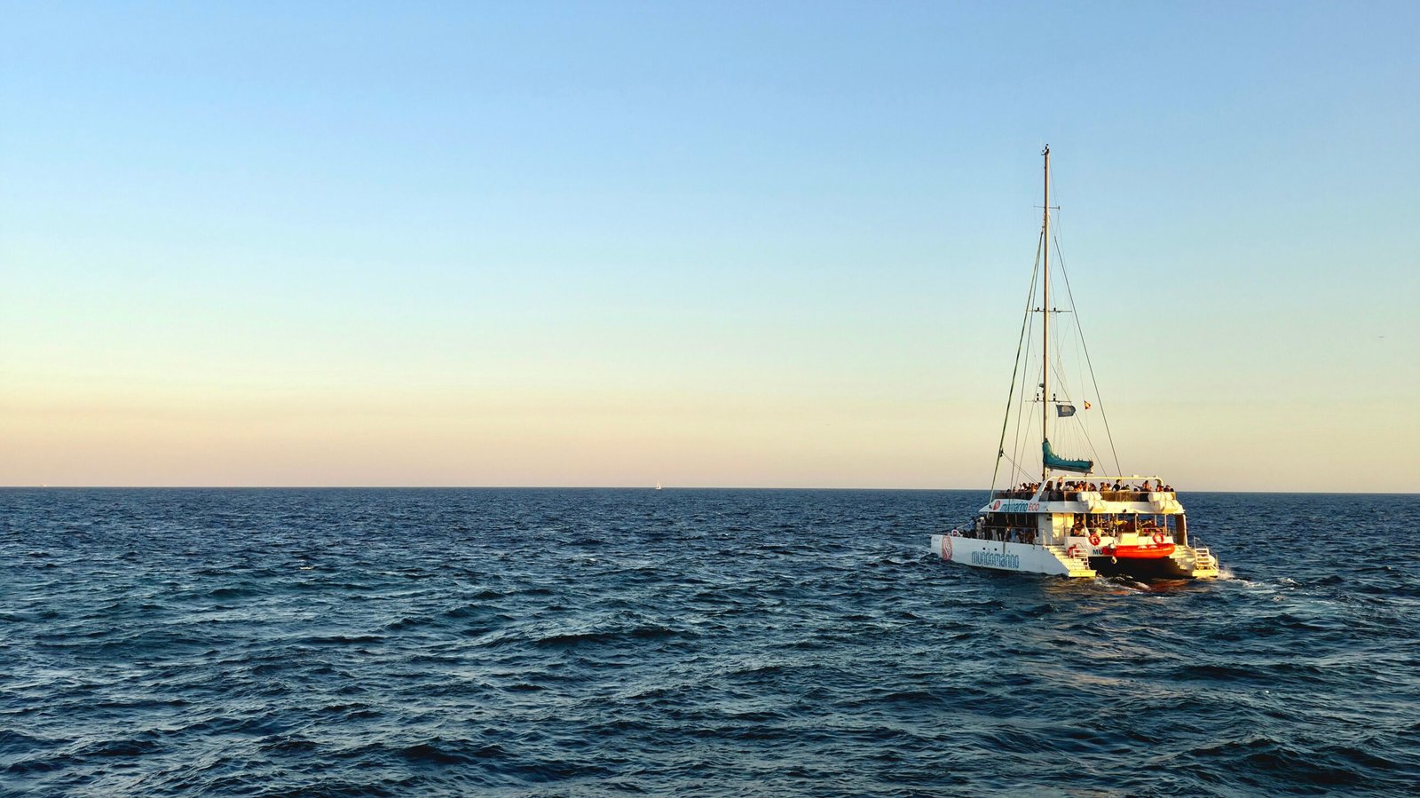 Catamarán con pasajeros navegando mar adentro al atardecer